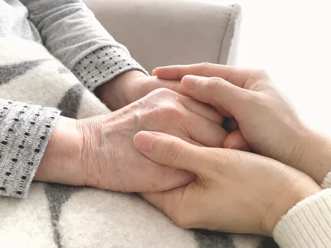 高齢の親の手に、子の手がそっと重ねられている写真