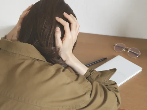 机に向かい、書類を前に考え込む人の後ろ姿